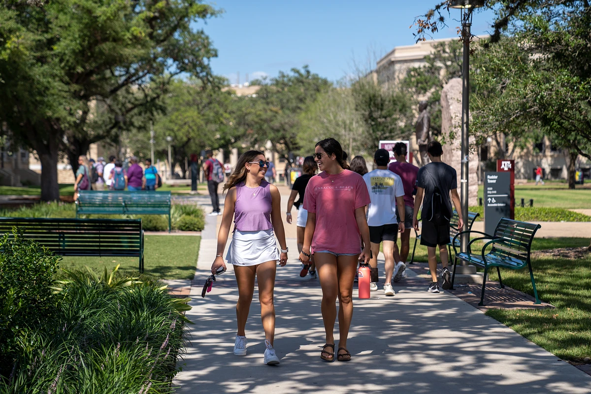 Two girls walking down military walk smiling at each other 