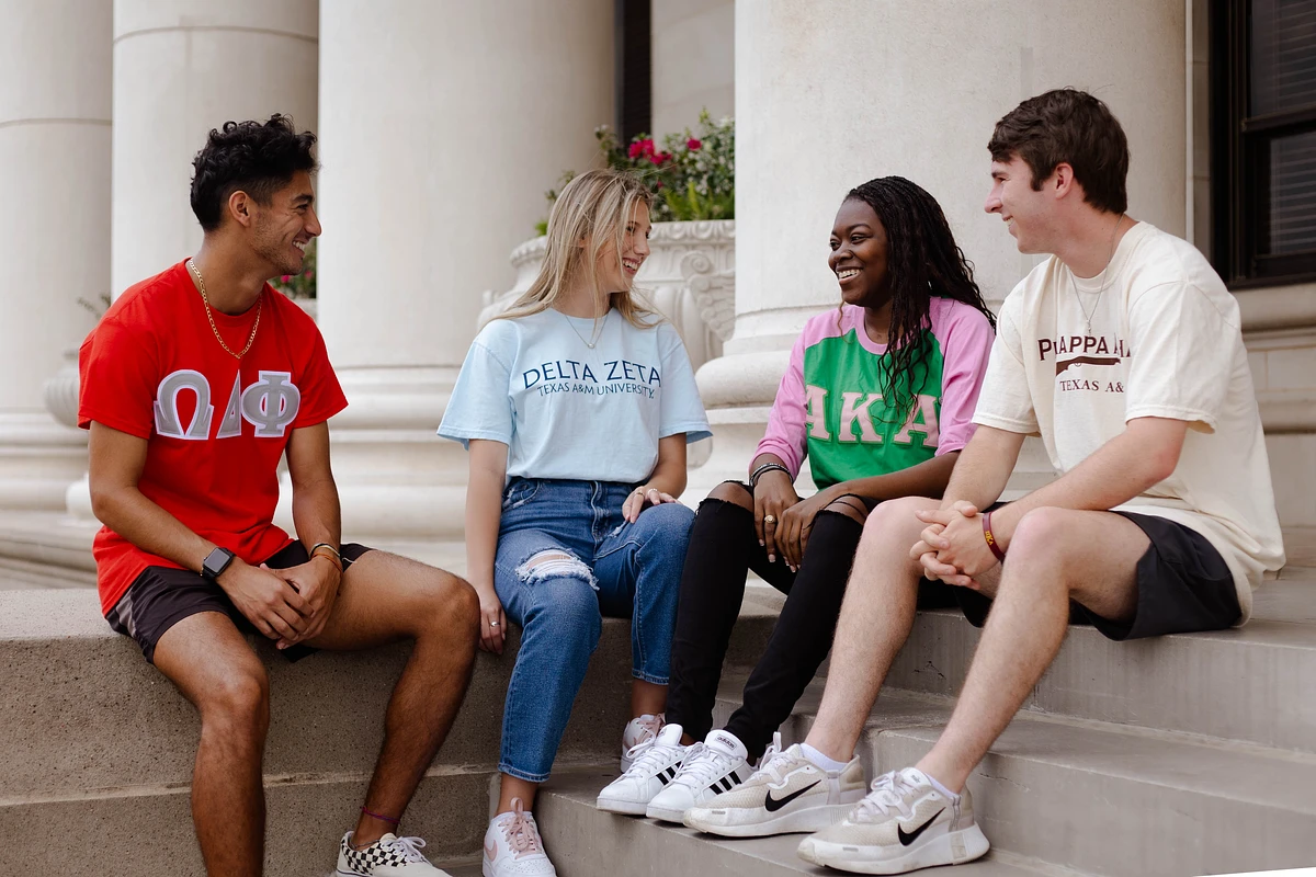 A group of students in fraternity and sorority shirts sitting in front of building
