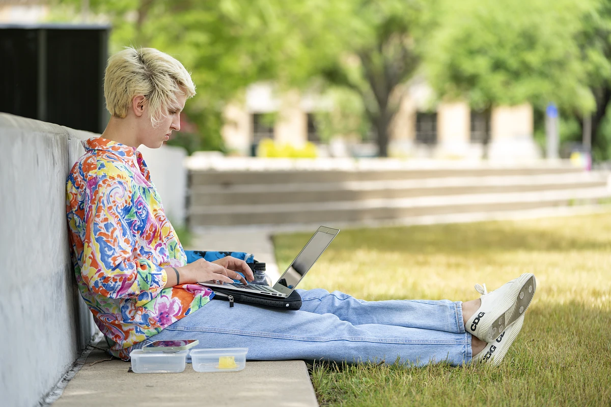 a student studying outside on their laptop. 