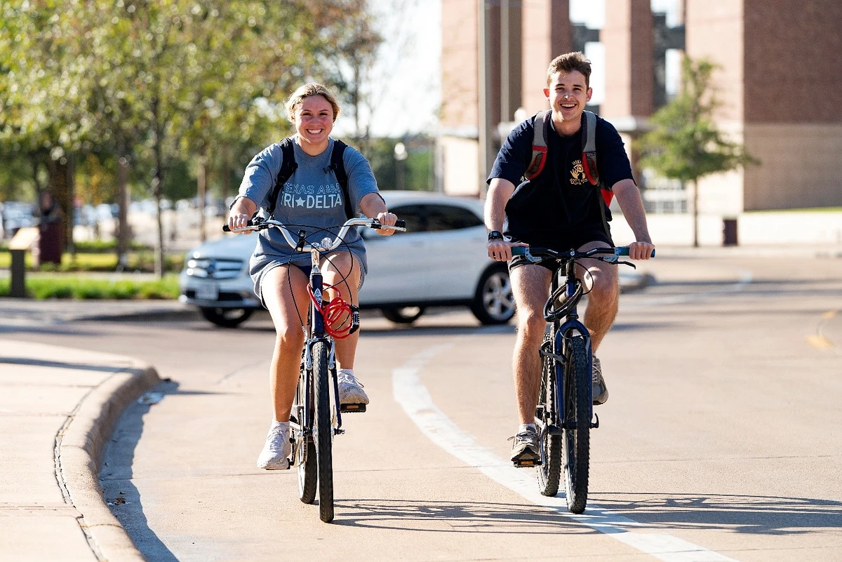 two student biking on campus smiling at the camera 