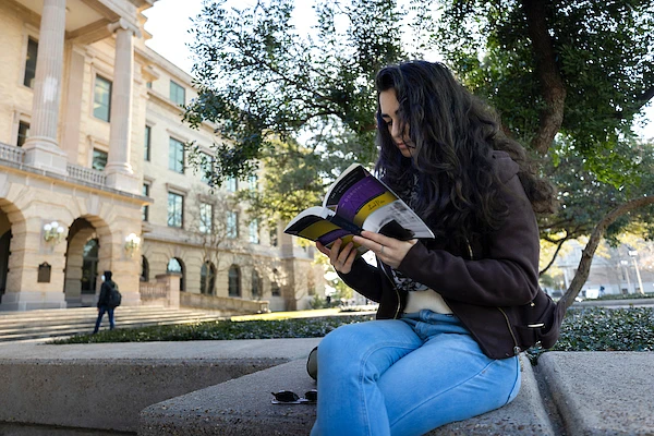 Girl sitting outside on the ledge, reading a book