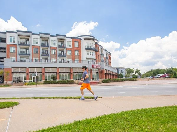 A student is jogging on a sidewalk in front of a multi-story building under a partly cloudy sky.