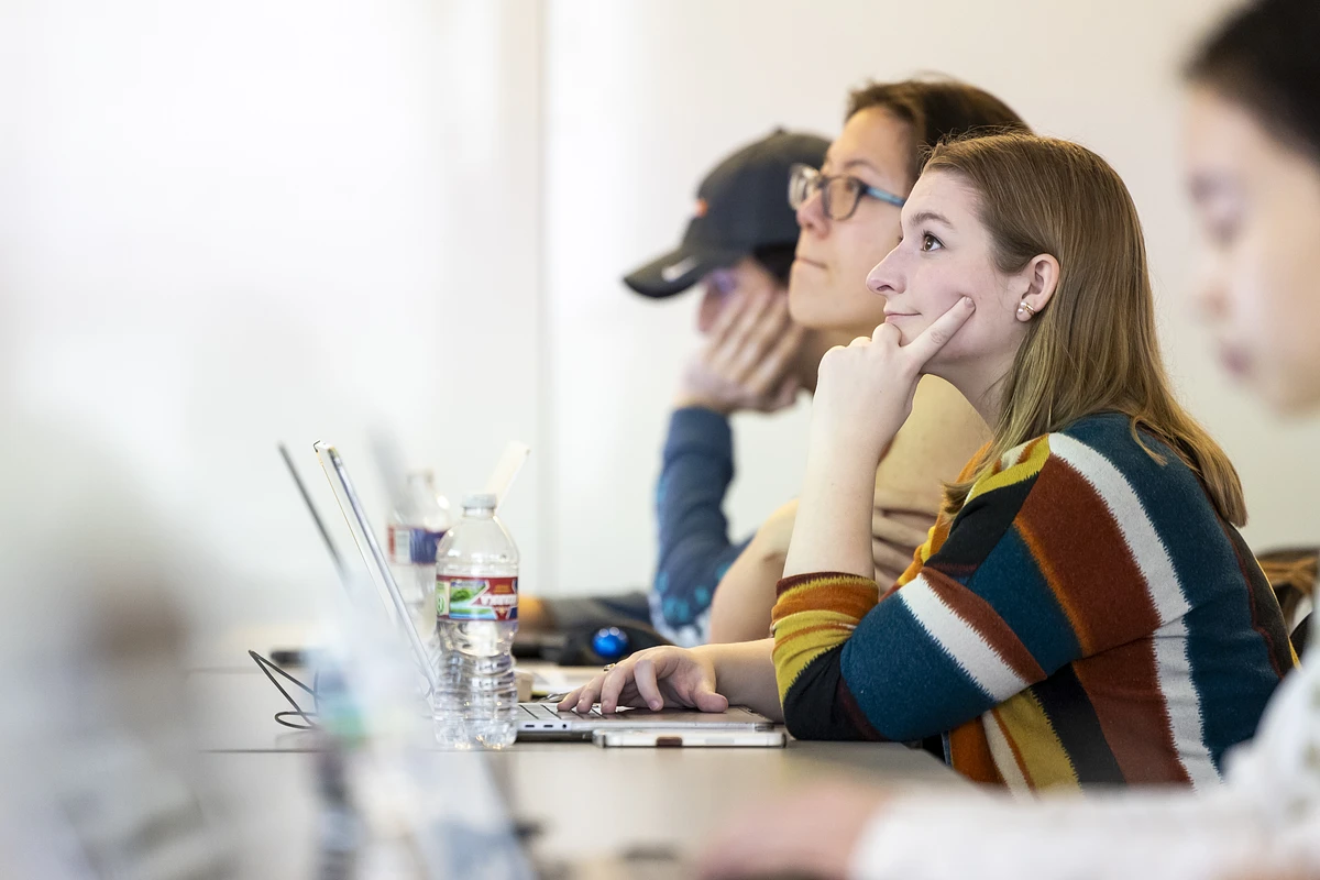 People attentively listening or watching something while using laptops in a classroom setting.