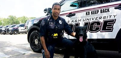 Texas A&M police officer with K9 in front of Texas A&M police car