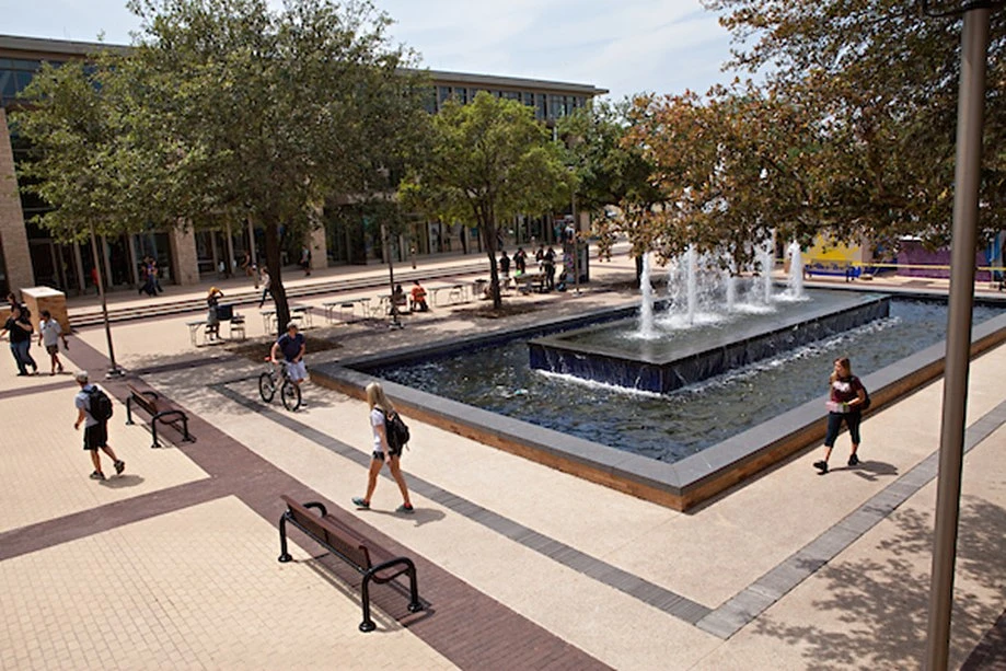 A photo of Rudder fountain on Texas A&M’s campus with students walking and biking around it 