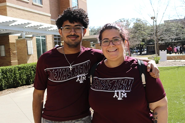Two people in matching Texas A&M shirts are smiling outdoors on a sunny day.
