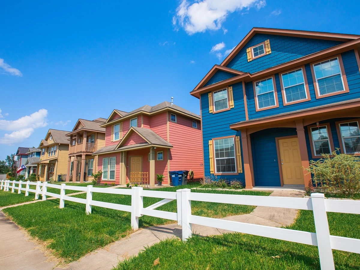 A row of brightly colored houses in a College Station neighborhood. Each house’s front yard is complete with a path to the front door and a white fence and gate.