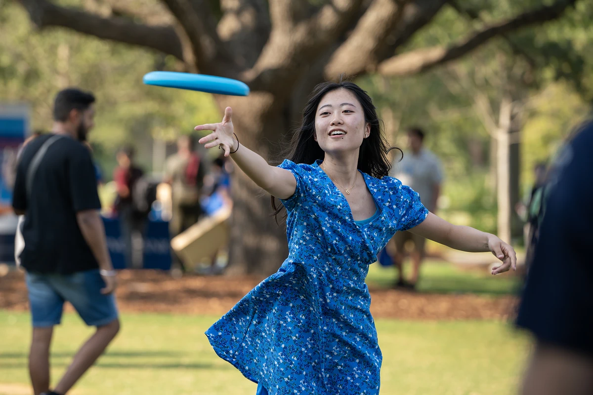 A woman in a blue dress is playing frisbee in a park.